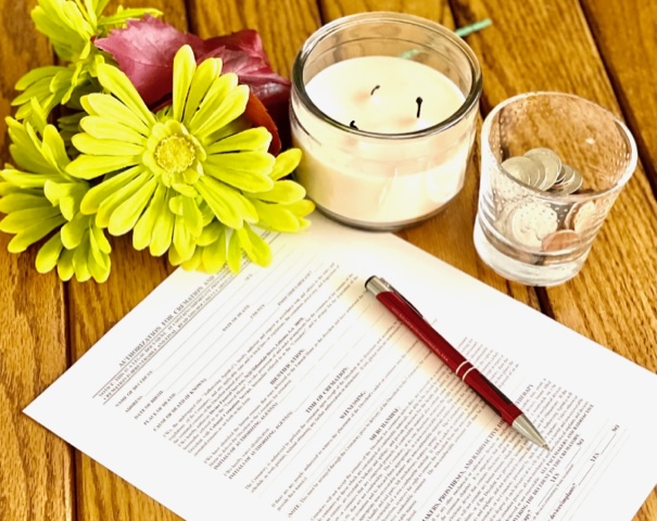 Photo of a candle on a desktop with an pen and cremation form